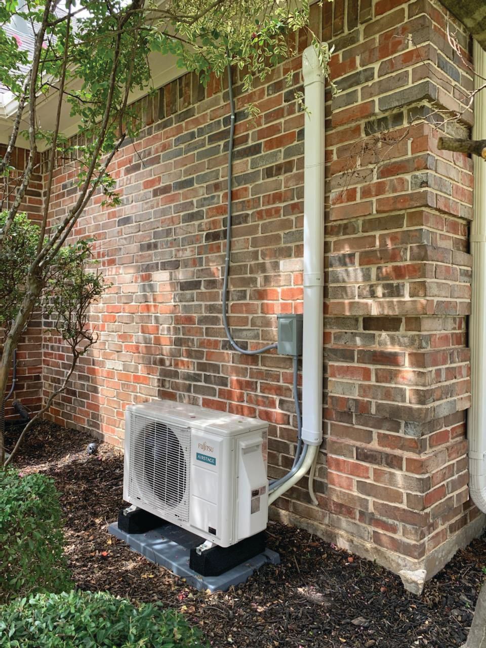 Three outdoor HVAC units lined up against a white fence in a backyard under bright sunlight