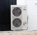 Outdoor air conditioning unit beside a black door and white brick wall