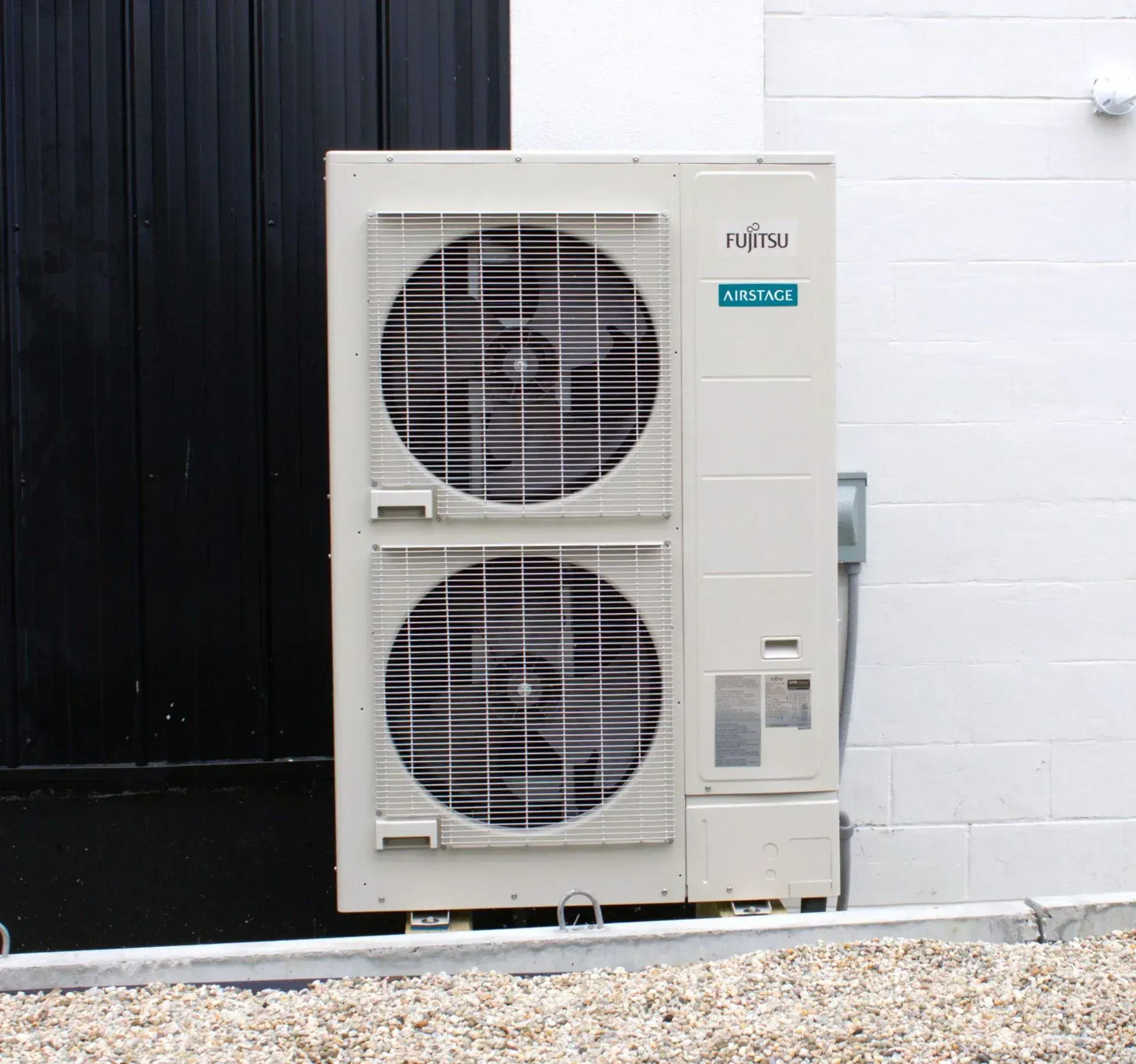 Outdoor air conditioning unit beside a black door and white brick wall