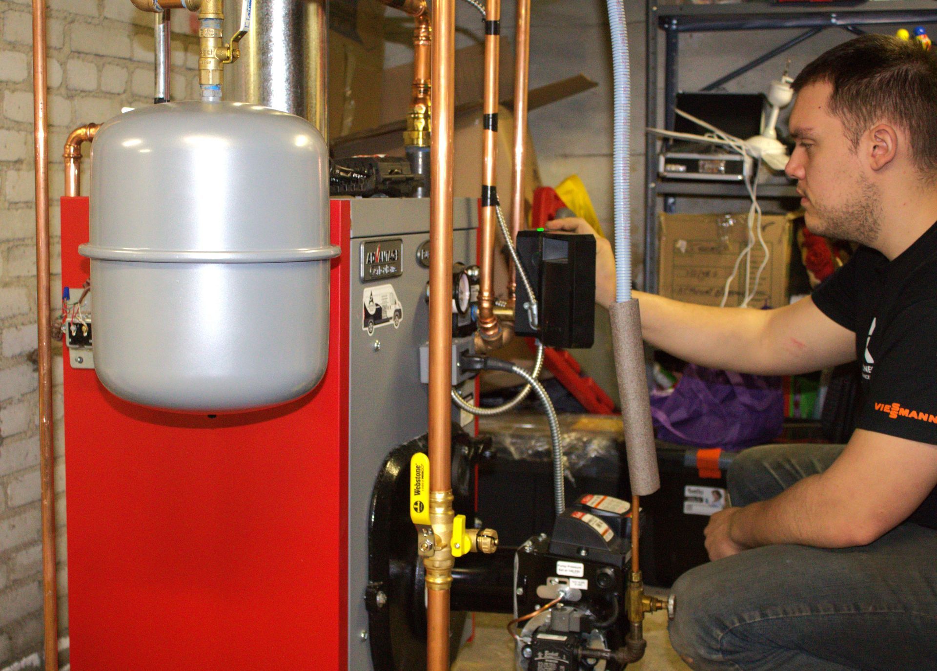 Technician adjusting equipment in a boiler room beside a red tank and silver pressure vessel