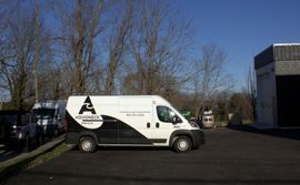 White delivery van parked in a lot beside trees and a building on a sunny day