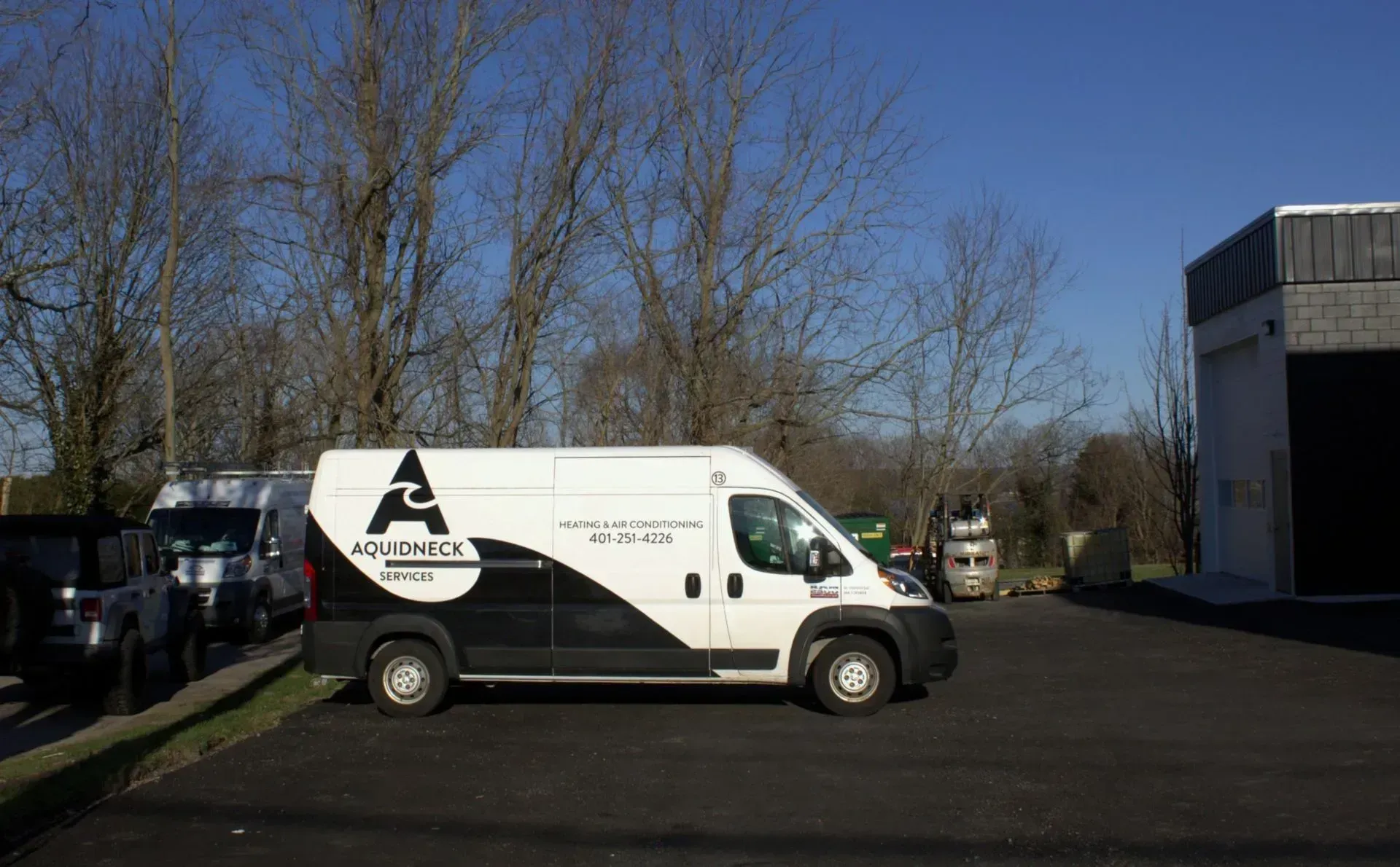 White delivery van parked in a lot beside trees and a building on a sunny day