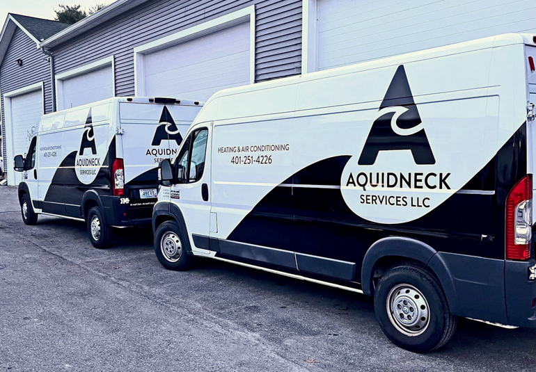 Two Aquidneck Irrigation vans parked beside a building, white and black with company logos.