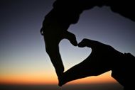 Hands forming a heart shape against a sunset sky