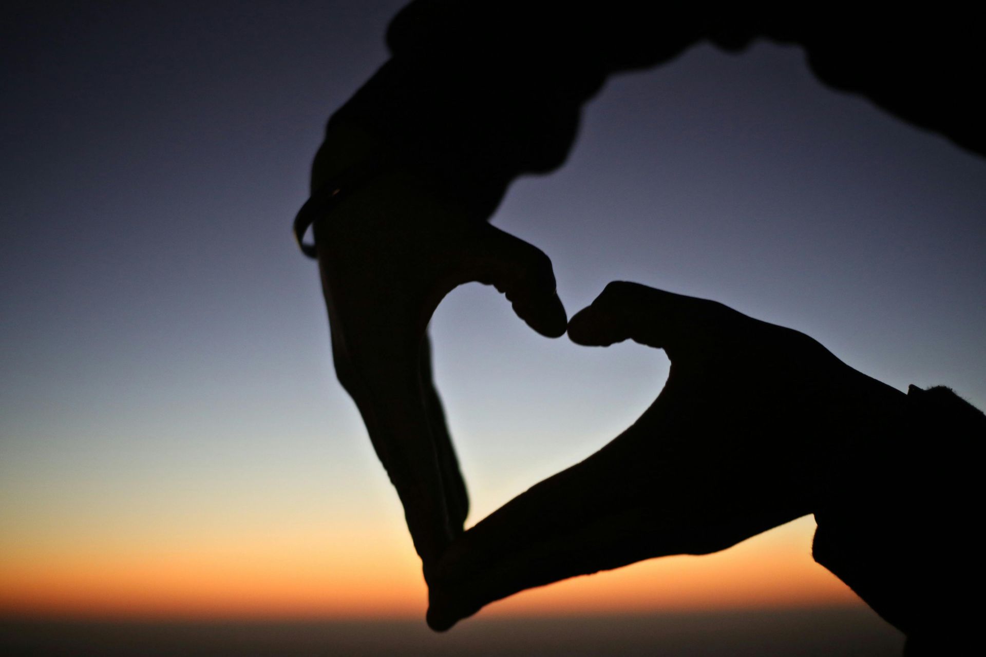 Hands forming a heart shape against a sunset sky
