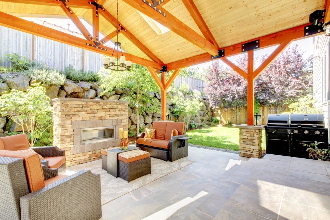 Covered patio with wicker seating, stone fireplace, and built-in grill in a landscaped backyard