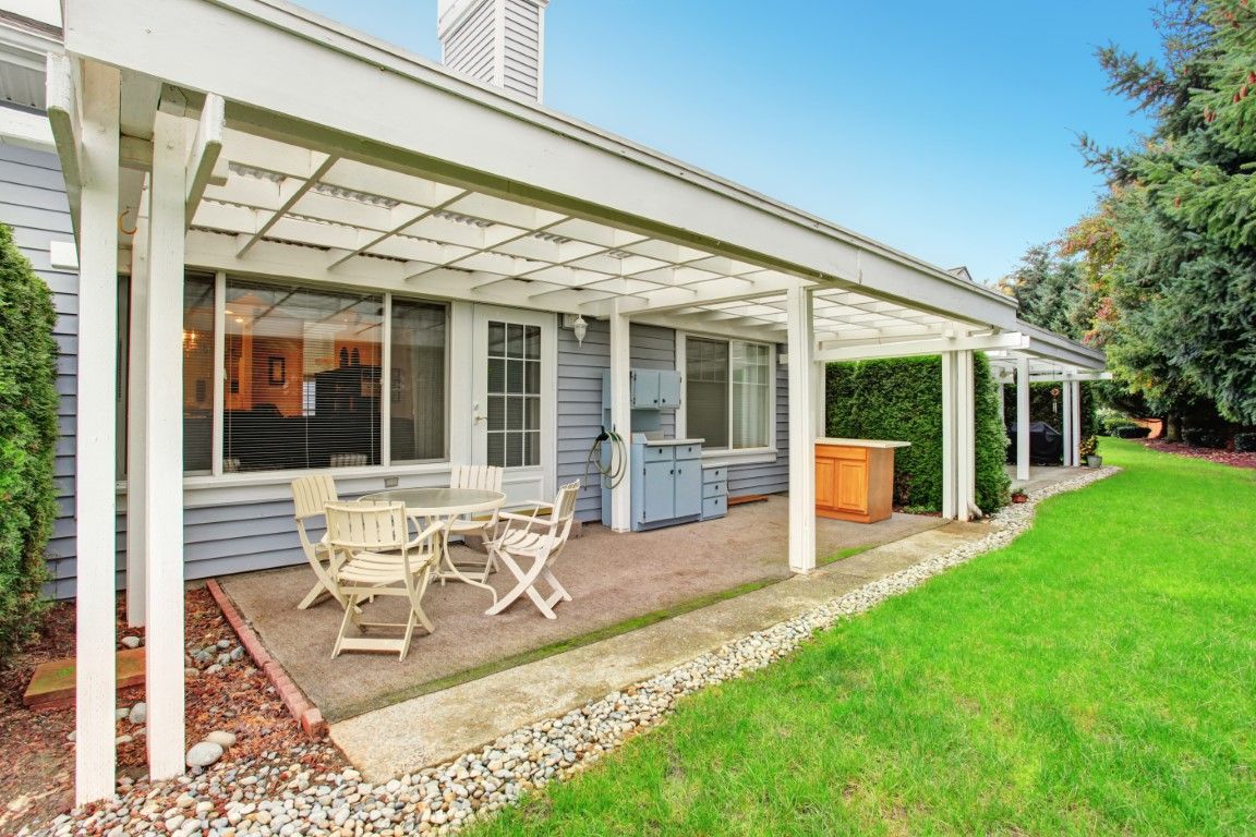 Covered patio with white outdoor furniture beside a house and green lawn