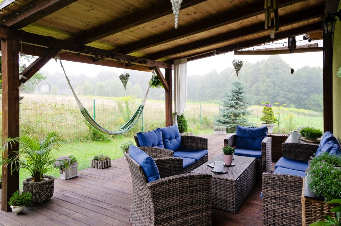 Covered patio with wicker seating and blue cushions overlooking a misty green yard