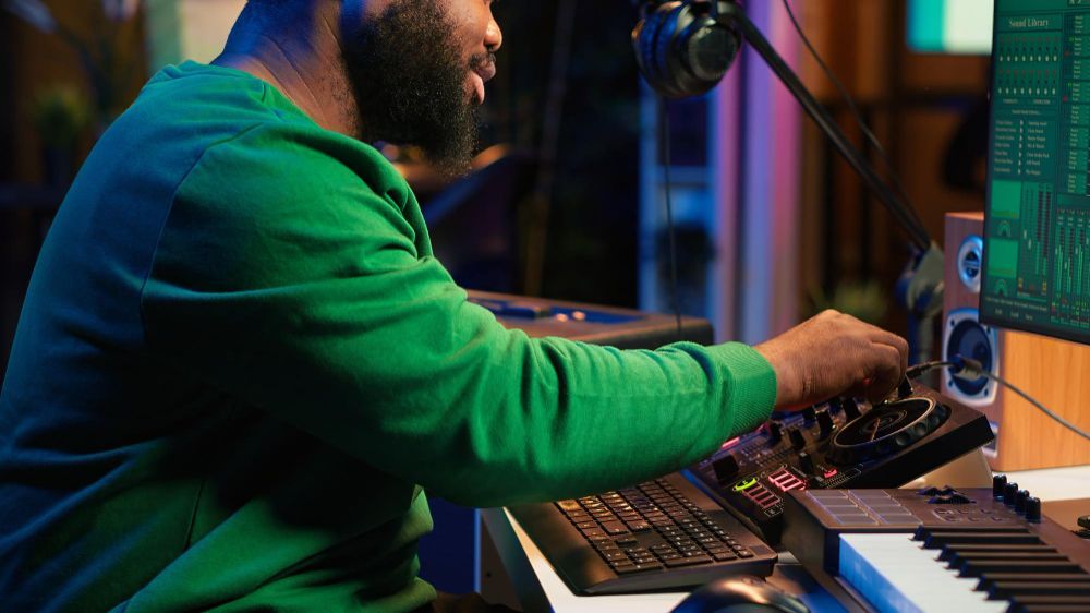 Person in green sweater adjusting audio equipment at a recording studio desk with a microphone and keyboard.