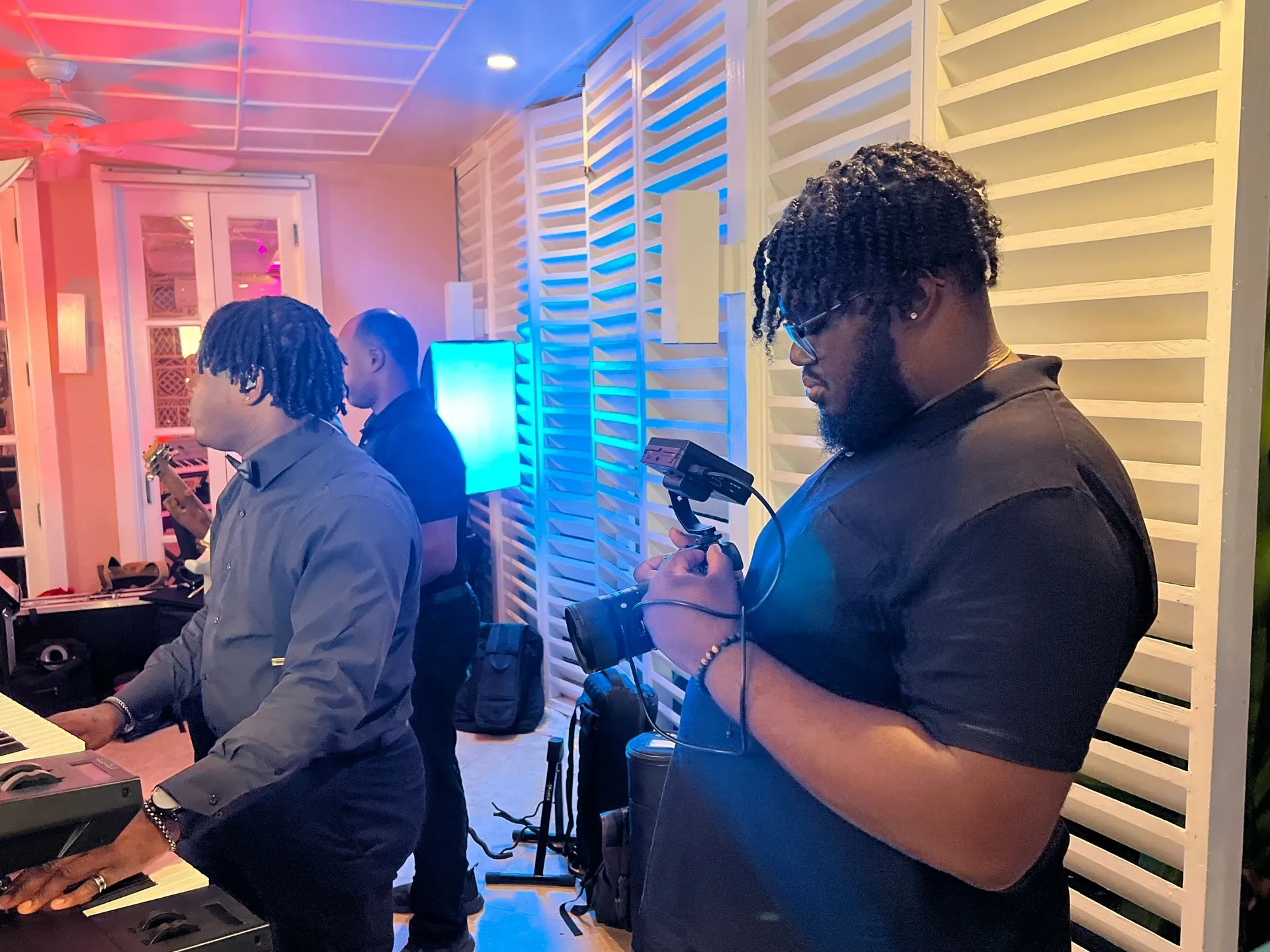 People in a studio with instruments and microphones, one person looking at a phone under blue and pink lights