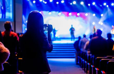 Audience watching a brightly lit stage performance in a blue-lit auditorium