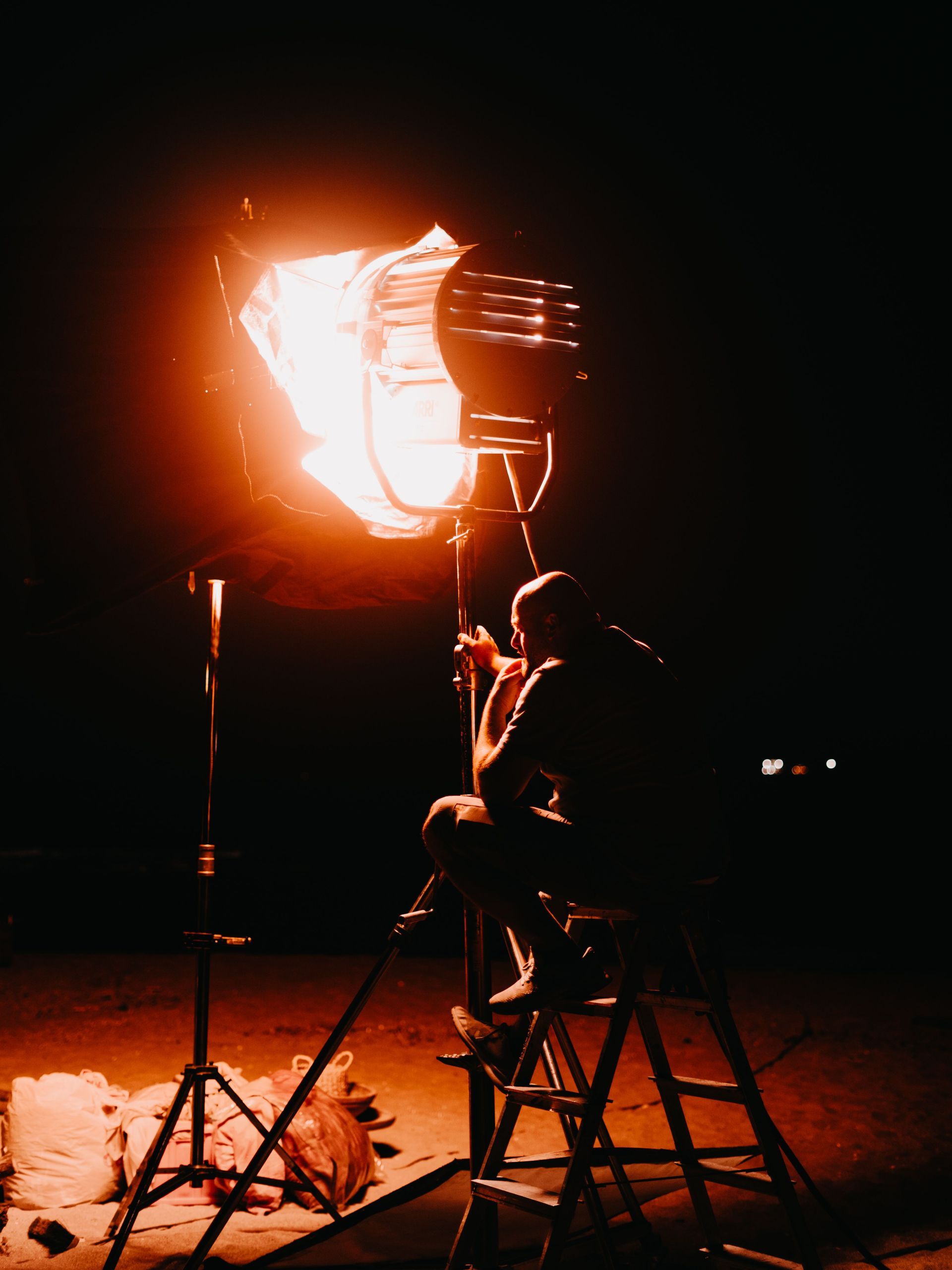 Person on a ladder adjusting a bright orange studio light in a dark room