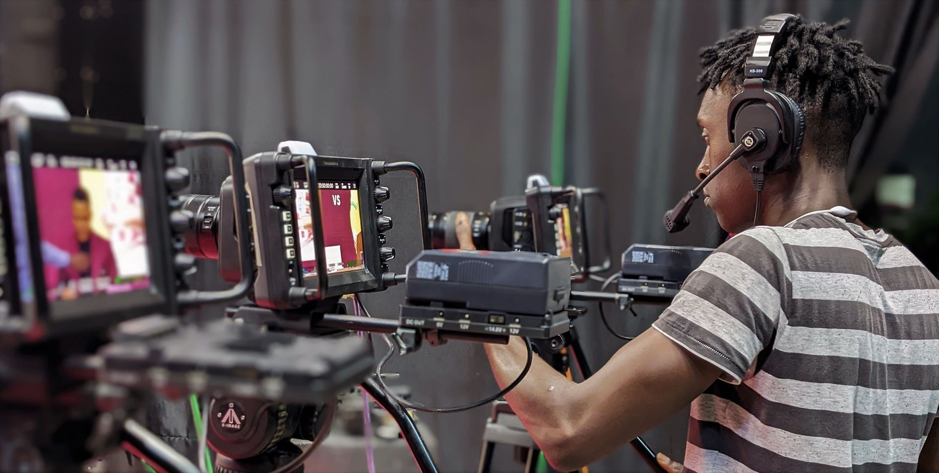 Video production crew filming a person at a row of cameras and monitors in a studio