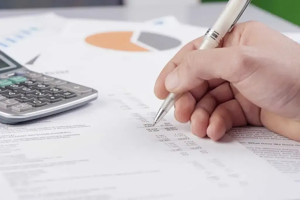 A person is writing on a piece of paper next to a calculator.