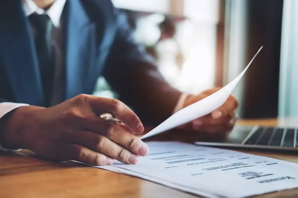 A man in a suit and tie is sitting at a table looking at a piece of paper.