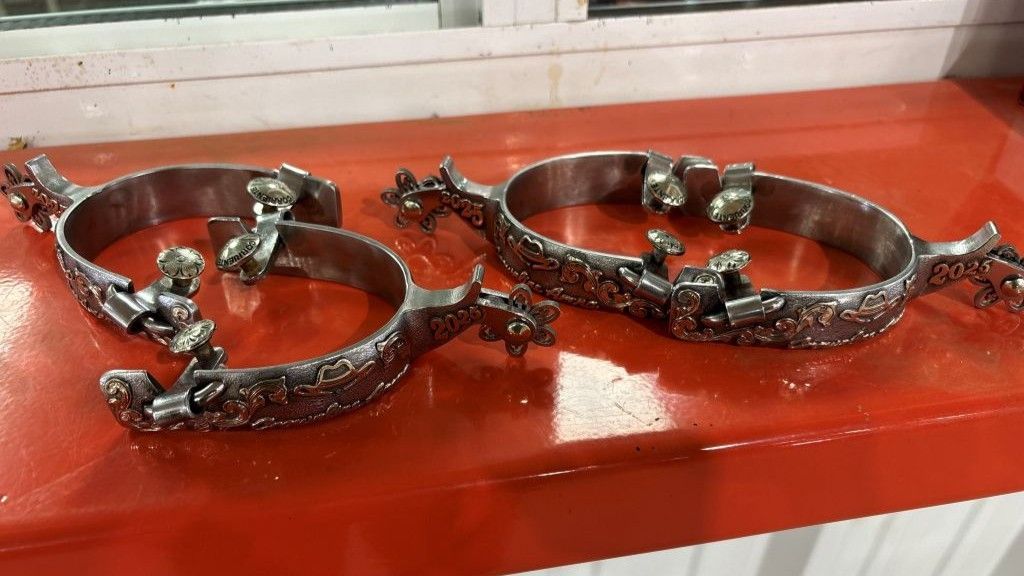 Silver spurs with ornate floral detailing, resting on a bright red surface.