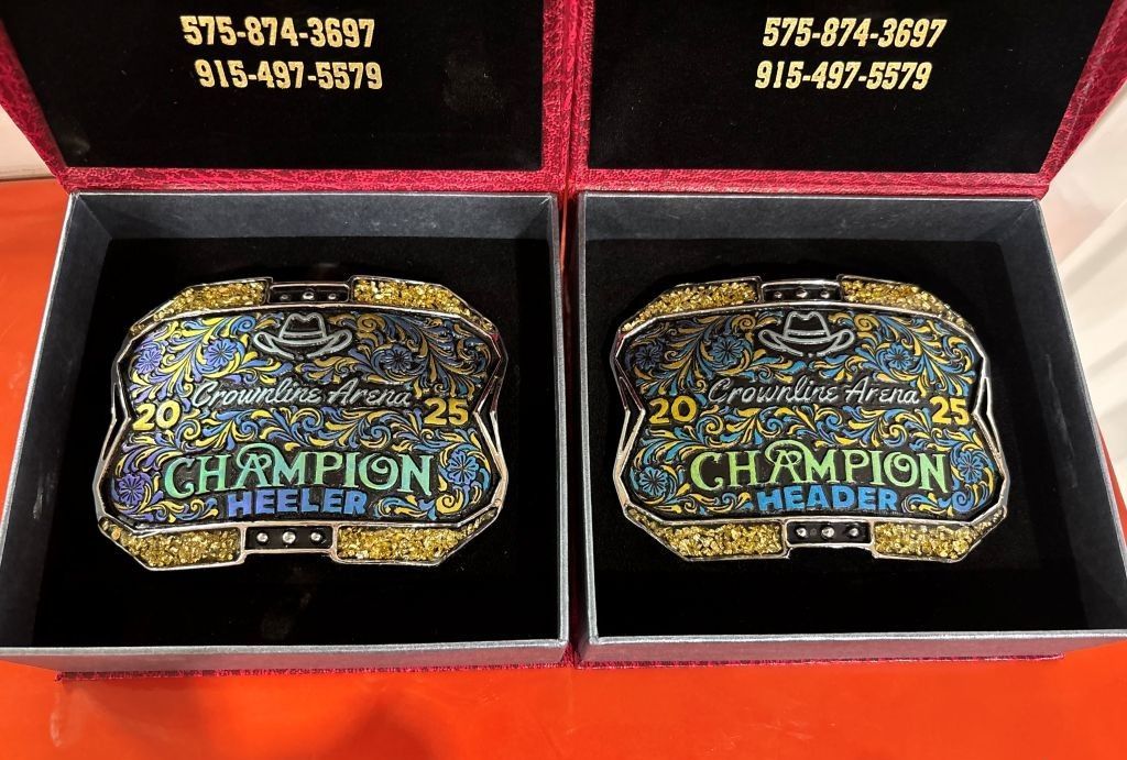 Two champion belt buckles in display boxes. Each is labeled