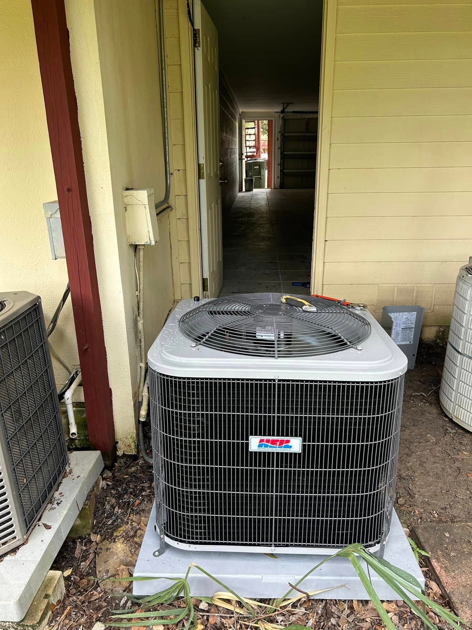 Outdoor air conditioner unit beside a beige house wall and walkway