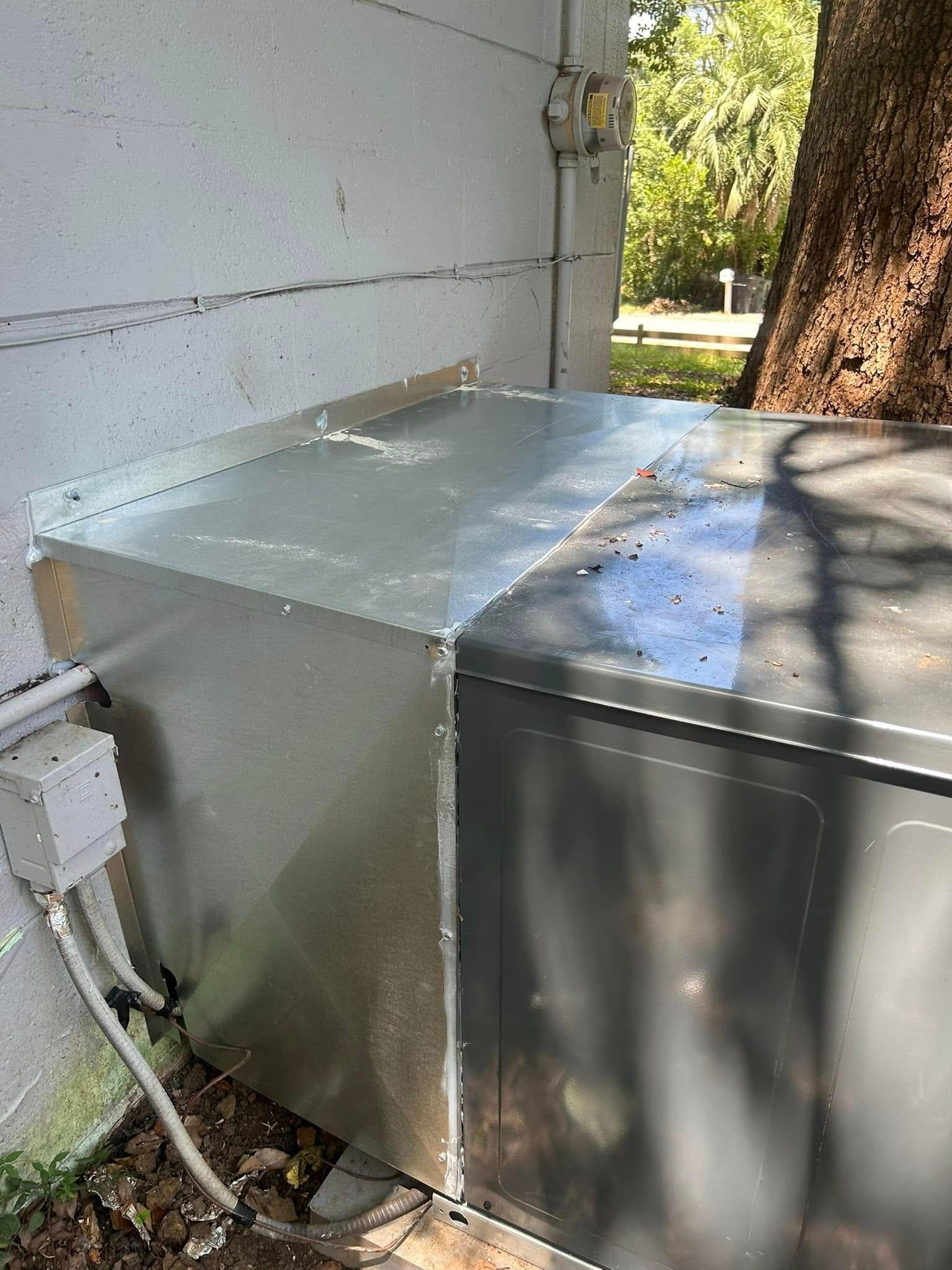 Metal outdoor HVAC units beside a house, with a large tree in the background.