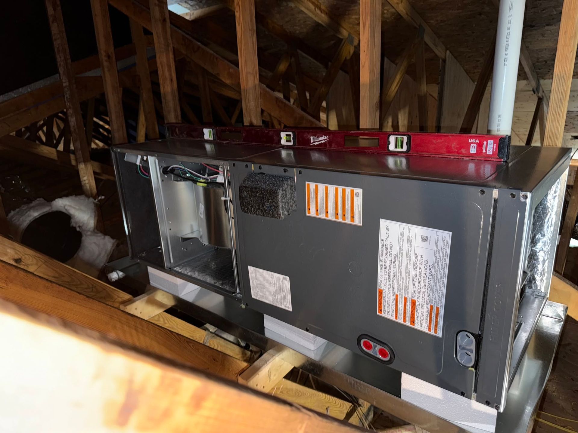 HVAC unit in an attic with exposed rafters and insulation, red ductwork on top