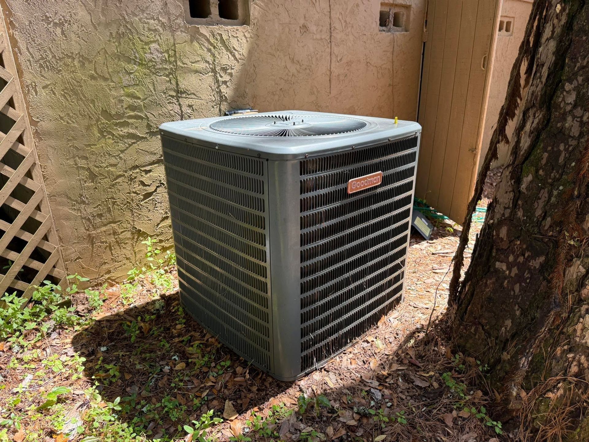 Outdoor central air conditioner beside a tree against a tan wall