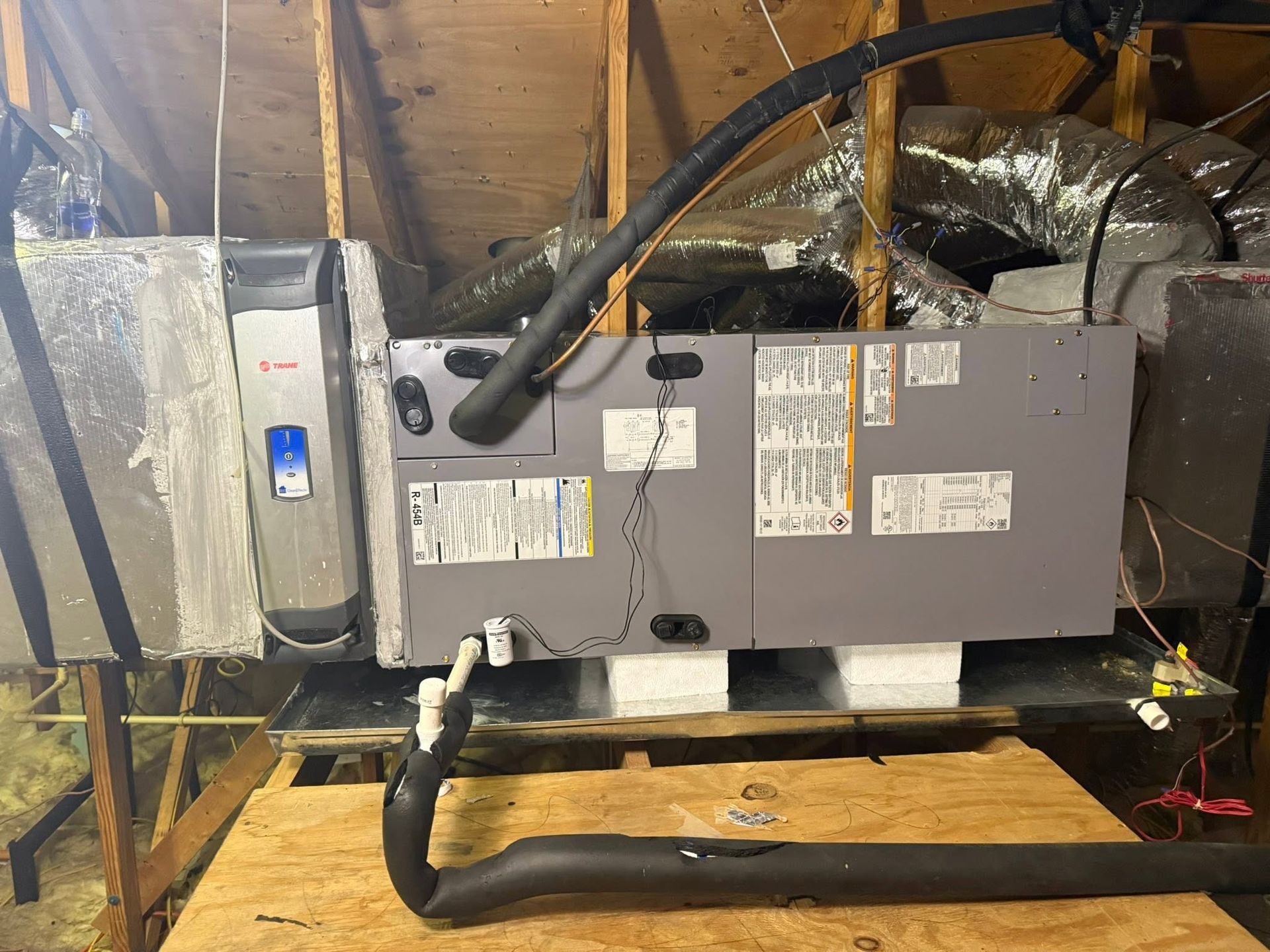 Gray HVAC unit with black insulated ducts installed in an attic space