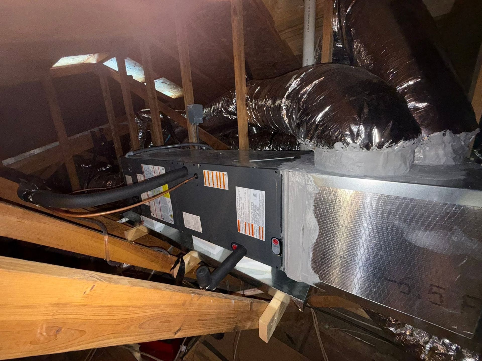 Attic HVAC unit with ductwork, wooden beams, and insulation under the roof