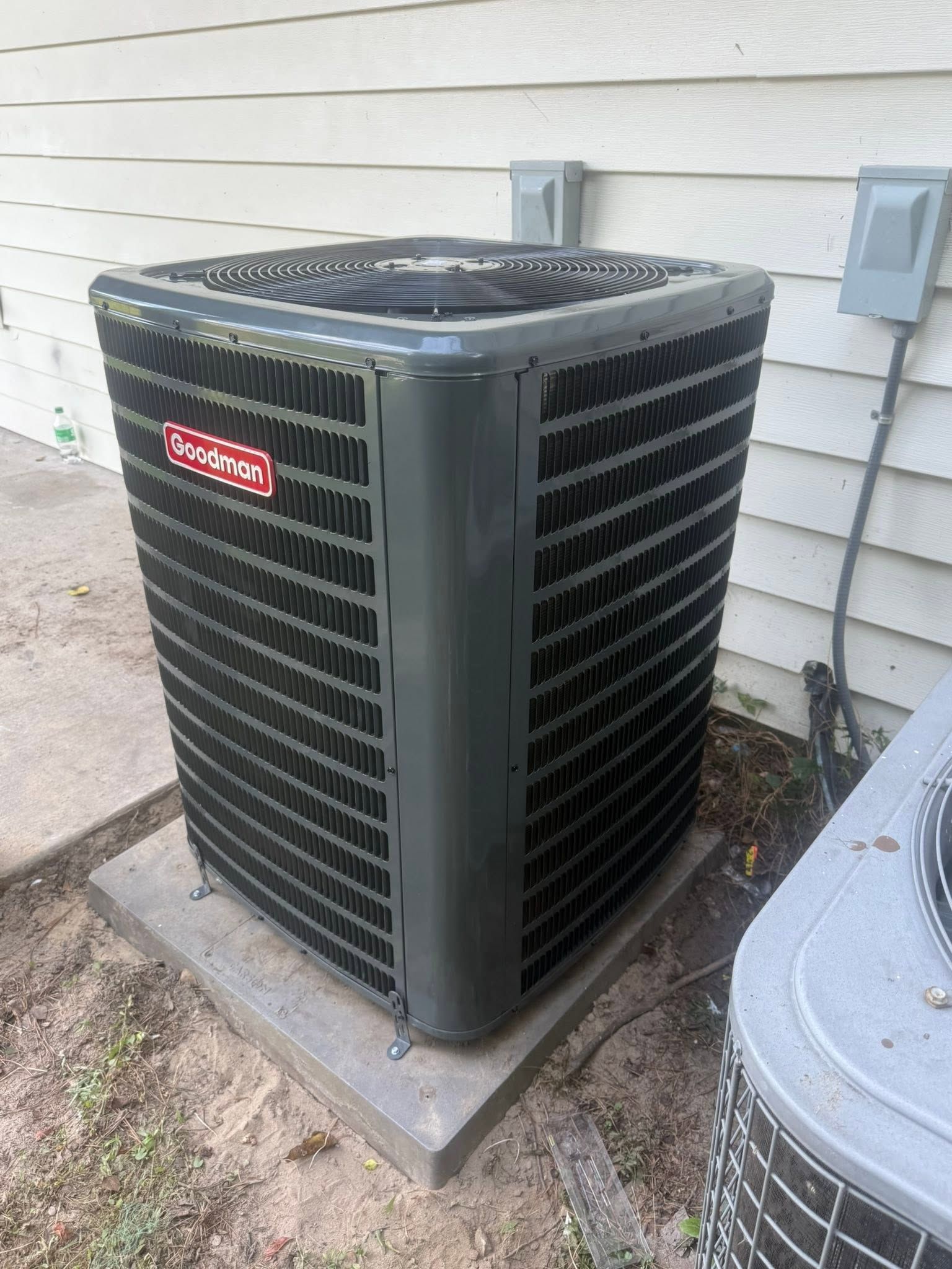 Outdoor central air conditioning unit beside a house wall and another AC unit.