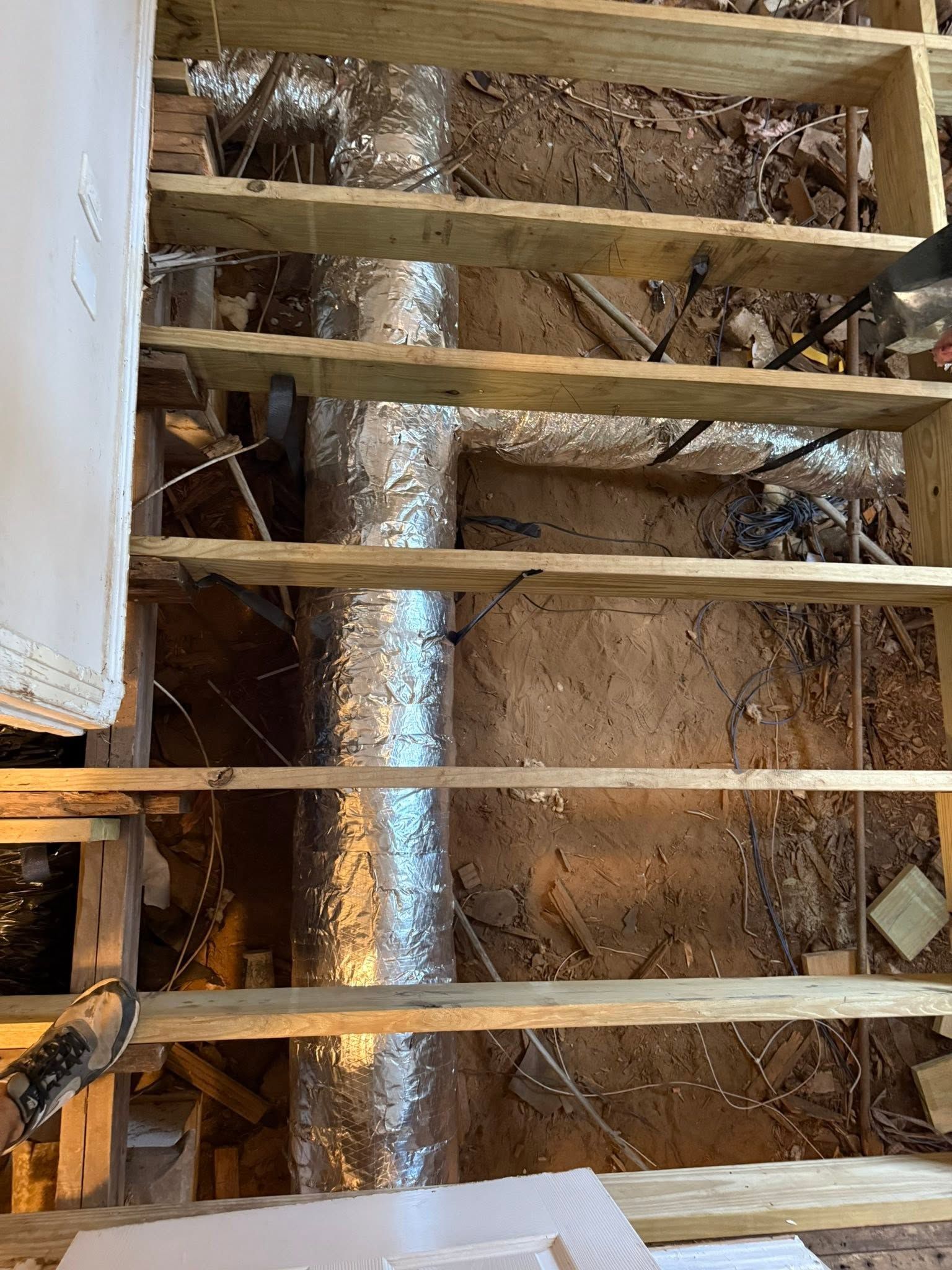 Exposed floor joists above a rough crawlspace with insulation and ductwork visible
