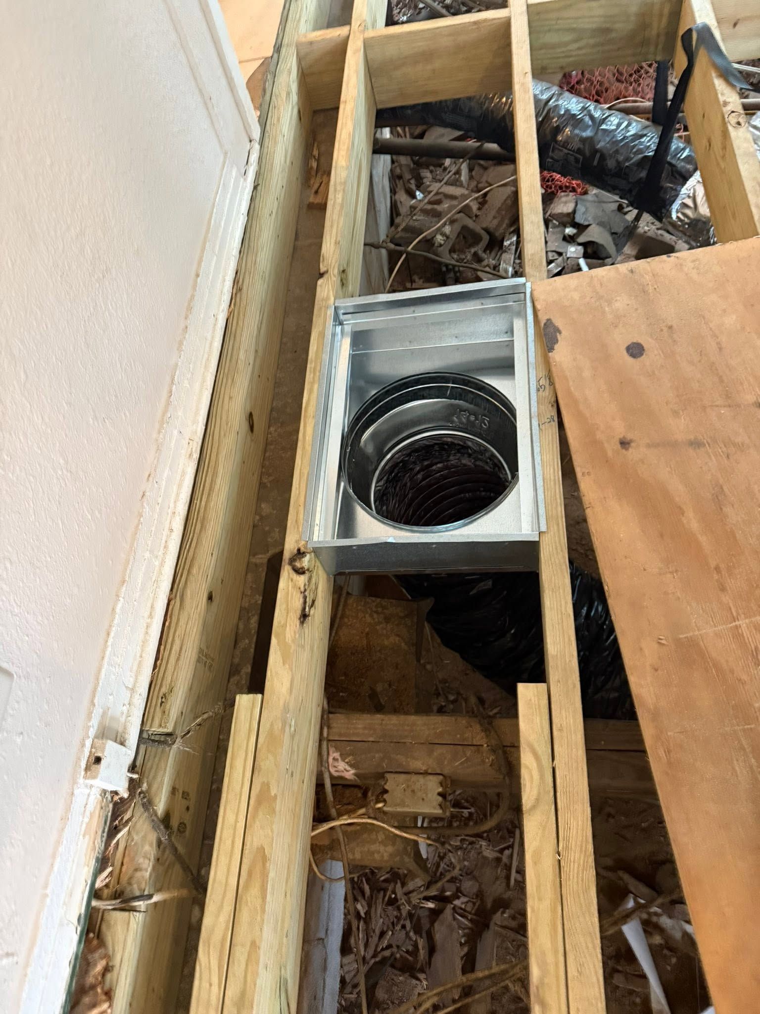 Rectangular metal duct opening between wooden joists in a construction area