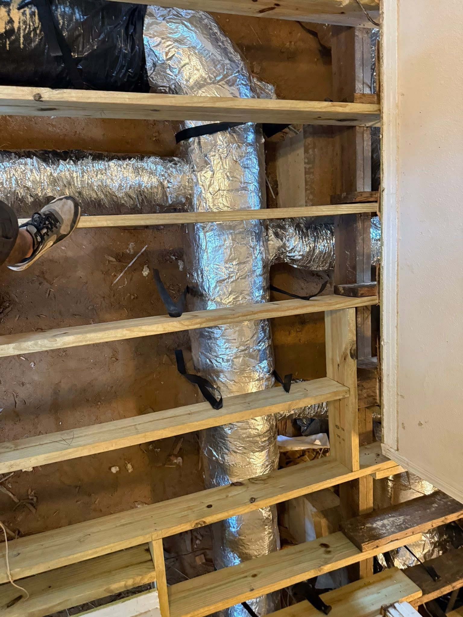 Exposed HVAC ductwork and pipes behind wooden framing in an unfinished wall area