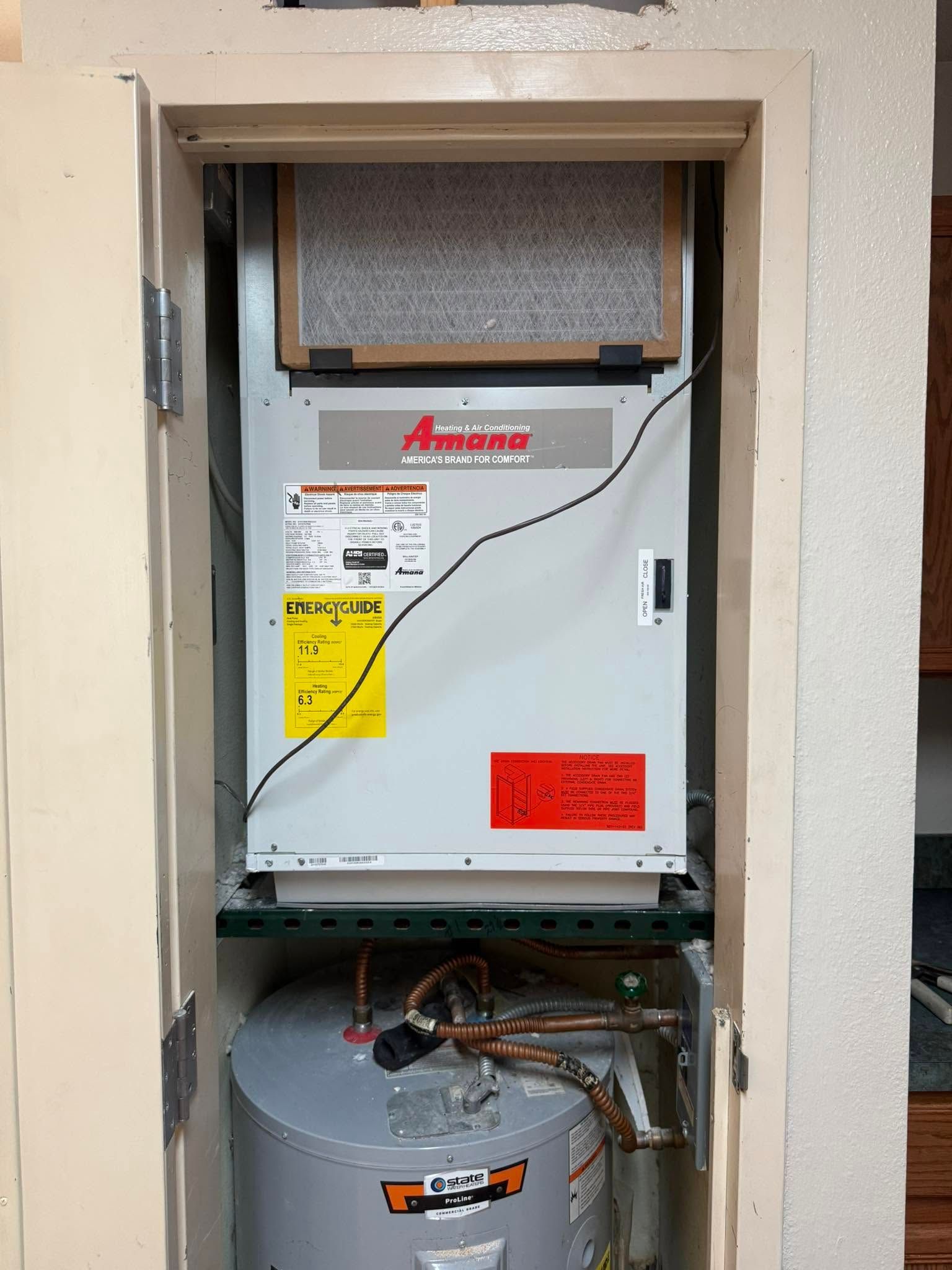Wall-mounted white HVAC unit in an open closet, with exposed wiring and a silver water heater below.