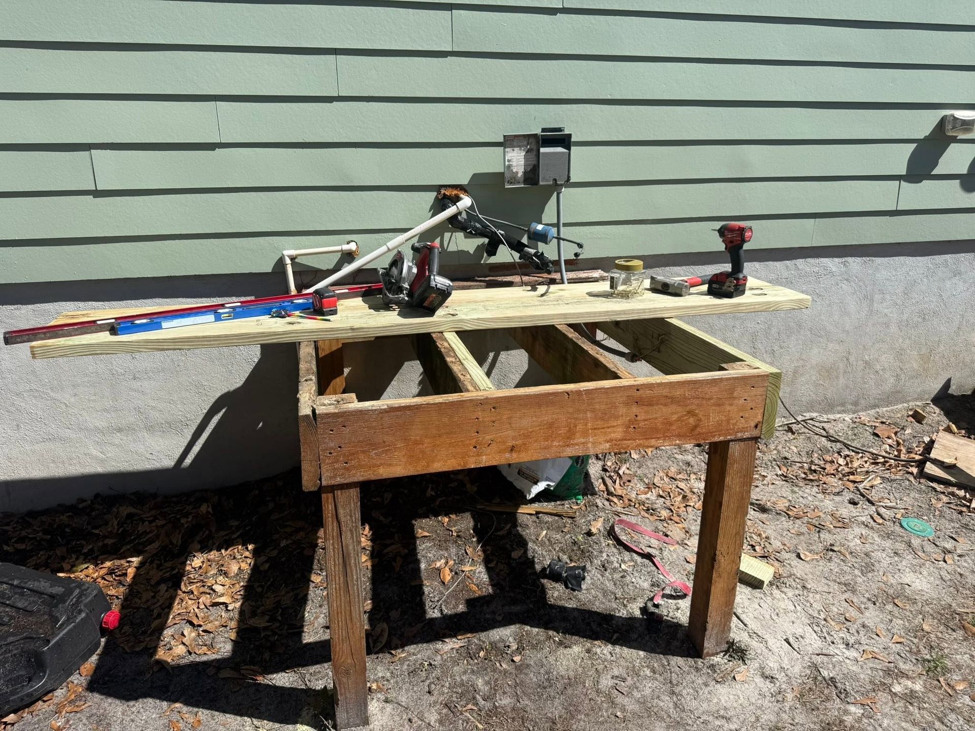 Homemade quadcopter on a wooden table outdoors beside a gray wall and dirt ground