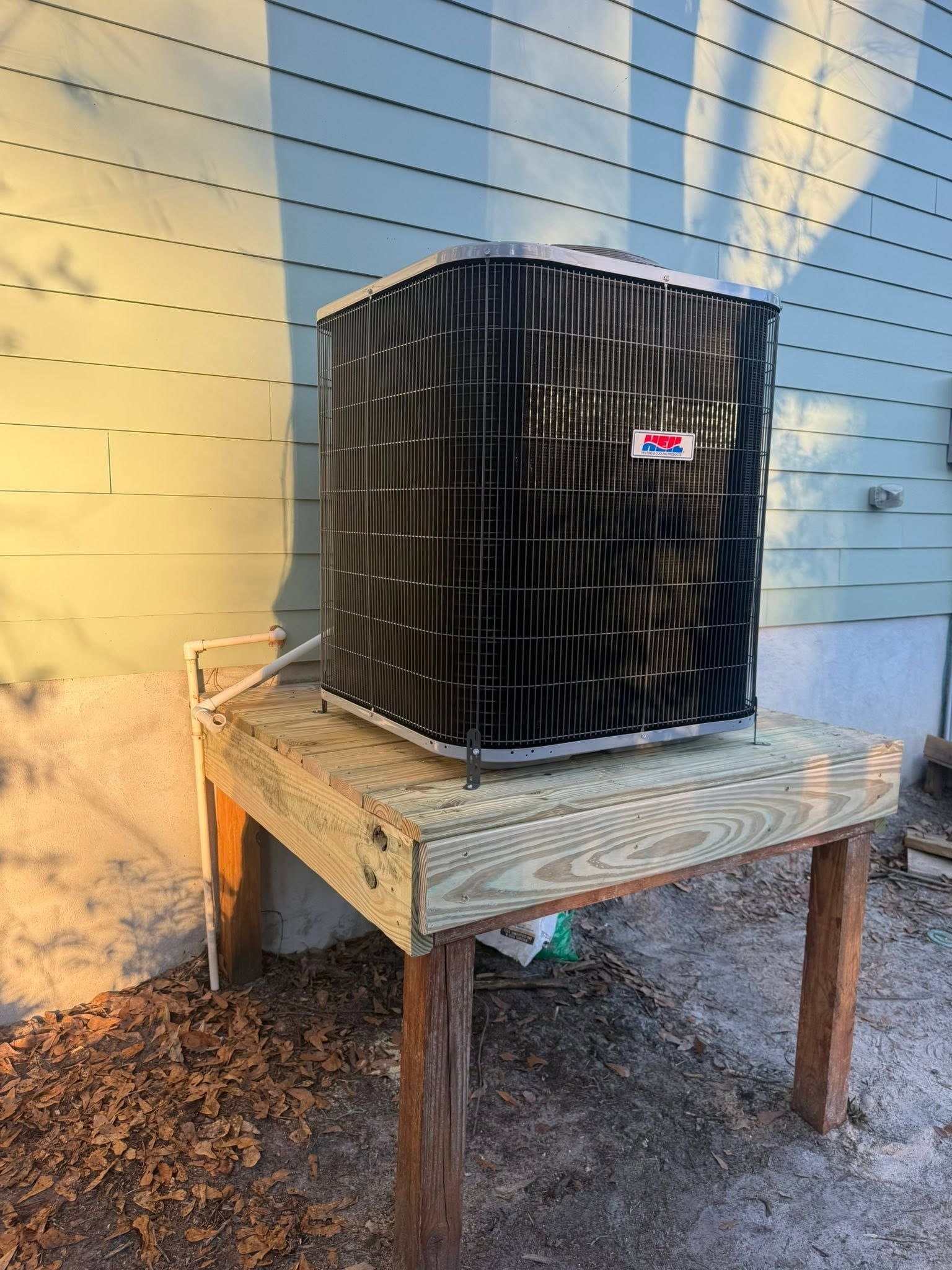 Black outdoor air conditioner unit on a wooden table against a blue and yellow wall.