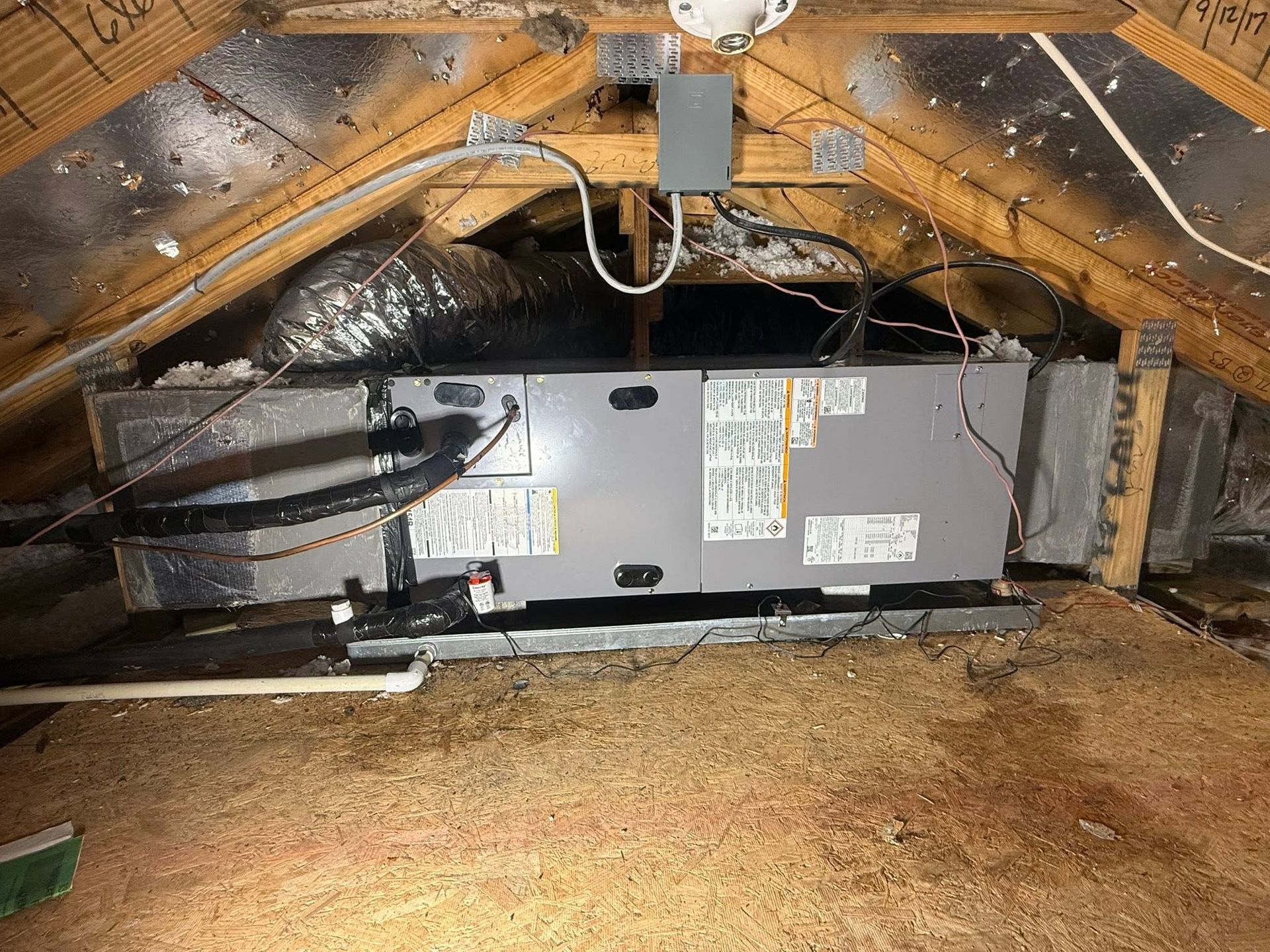 HVAC unit in an attic with exposed ductwork and insulation under the roof rafters