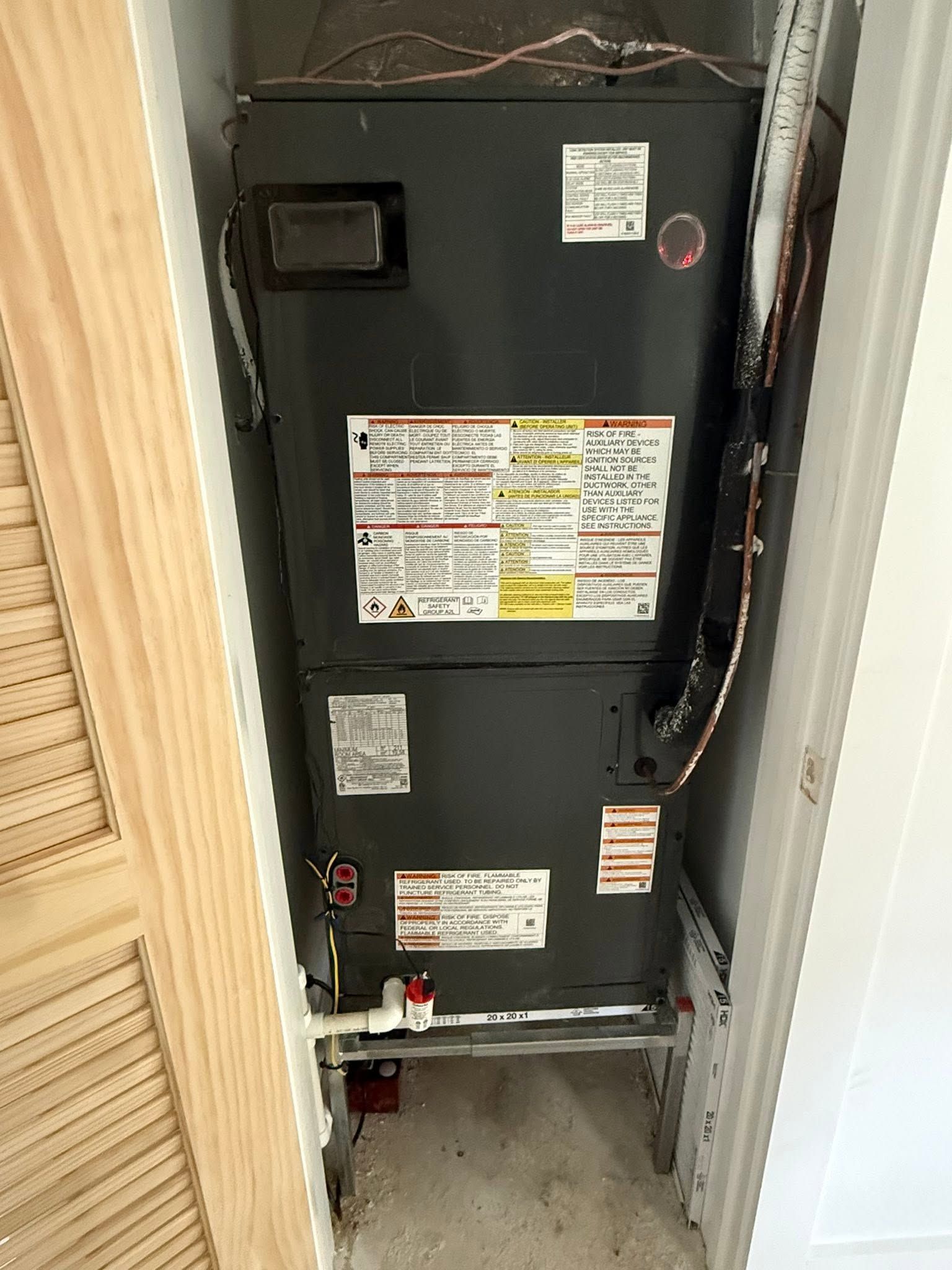 Open furnace unit in a closet, with labels and pipes visible.
