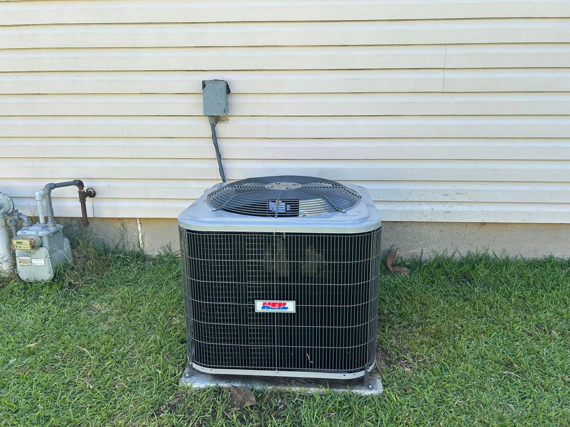 Outdoor air conditioner unit beside a beige house wall on grass