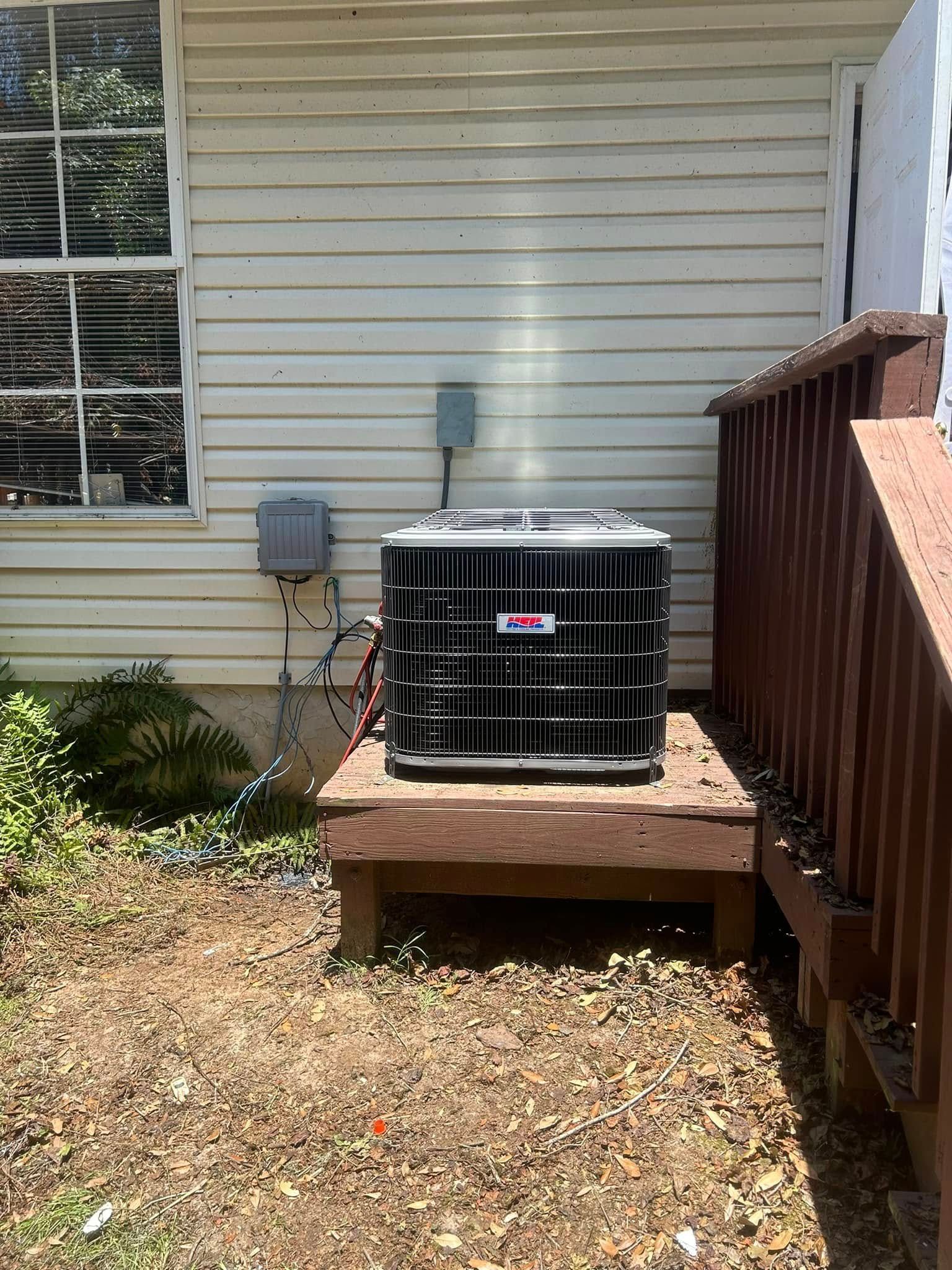 Black outdoor generator on a wooden platform beside a house and deck railing.