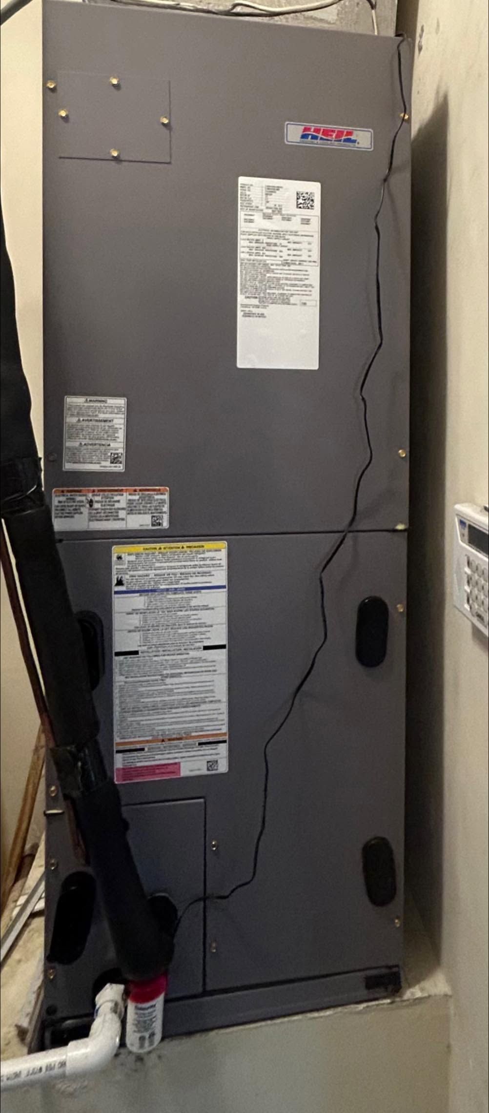 Gray HVAC unit in a narrow utility closet with posted notices and visible cables.