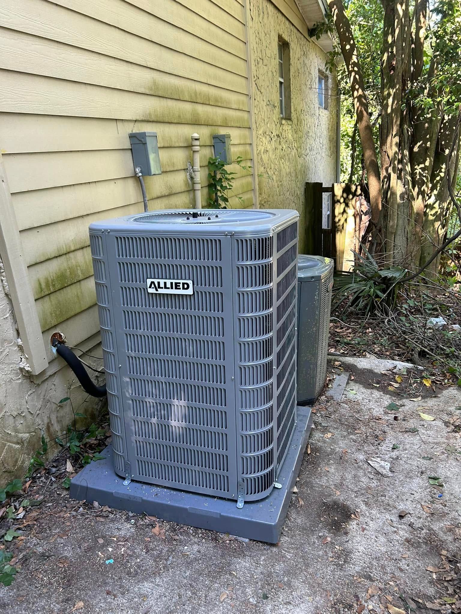 Outdoor air conditioner unit beside beige house siding on gravel near bushes