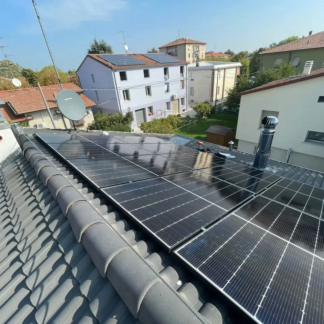 Pannelli solari installati su un tetto di tegole in una giornata di sole. Sullo sfondo si vedono delle case.