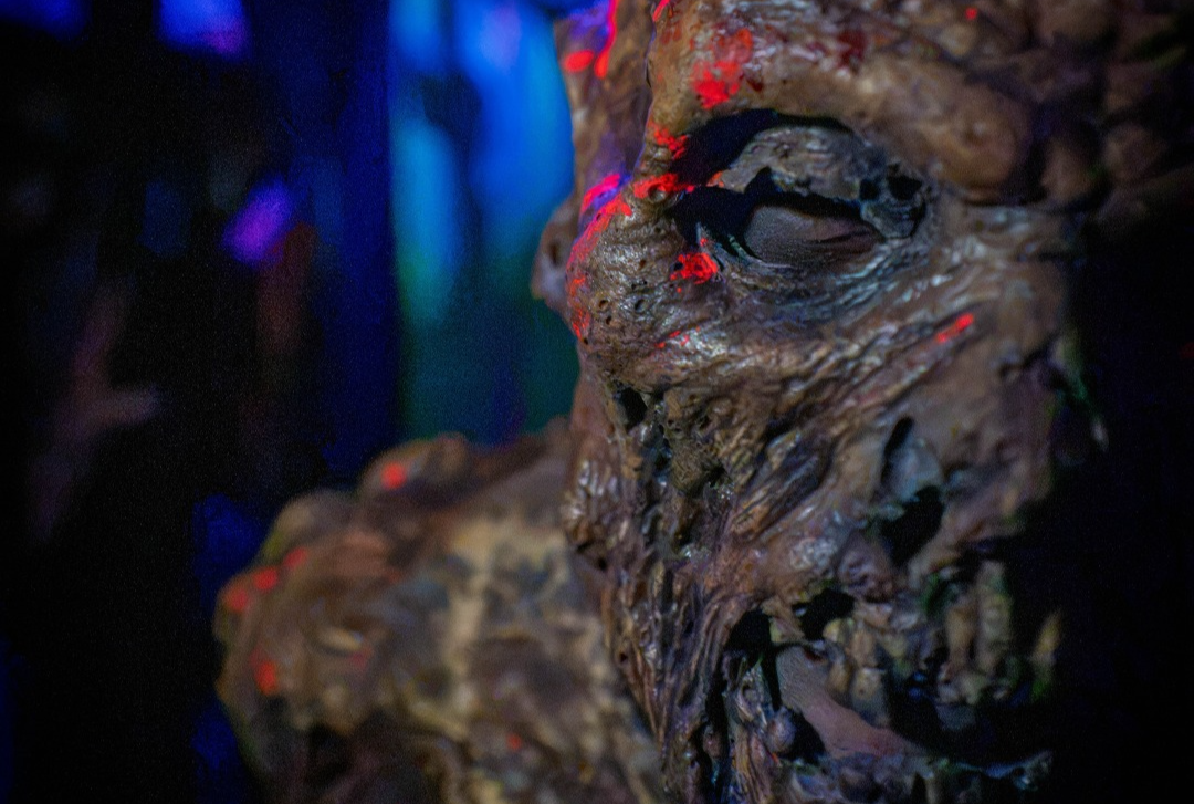 Close-up of a grotesque monster face with red eyes in dark blue-purple lighting