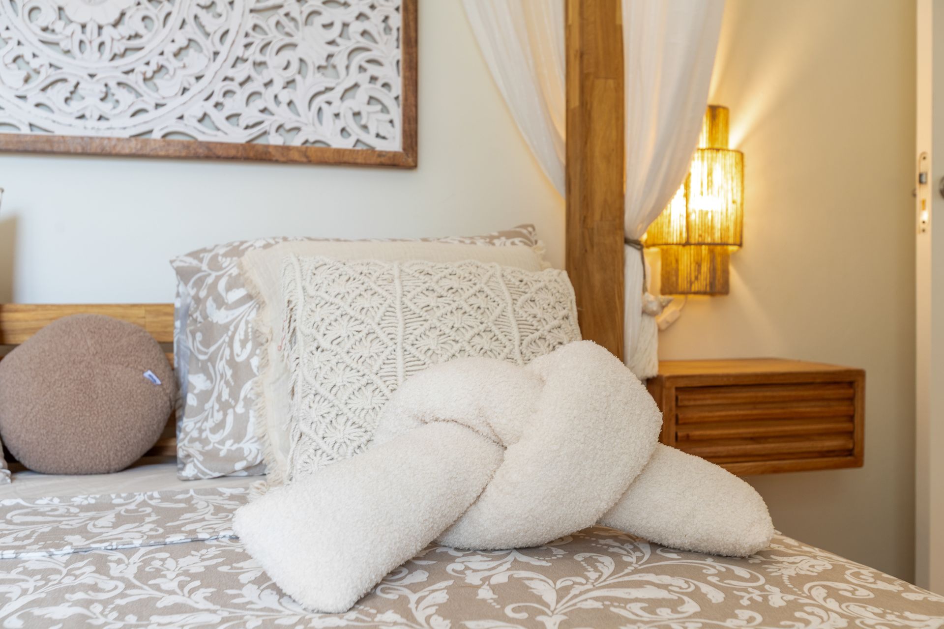 Slaapkamer met crèmekleurig en beige beddengoed, sierkussens, een houten hoofdbord en houtsnijwerk aan de muur.