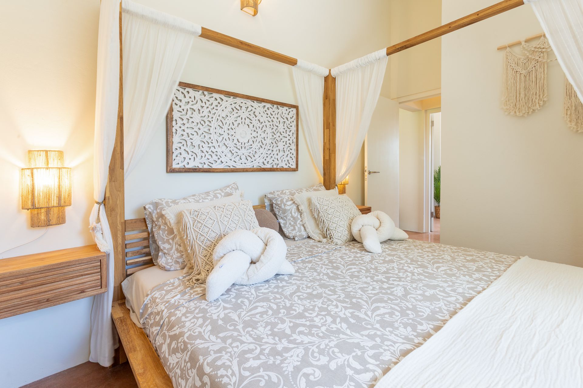 Slaapkamer met hemelbed, sierkussens, houten hoofdbord en wandlampen.