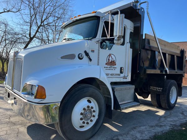 White dump truck parked outdoors on a sunny day, front-left view with a black cargo bed