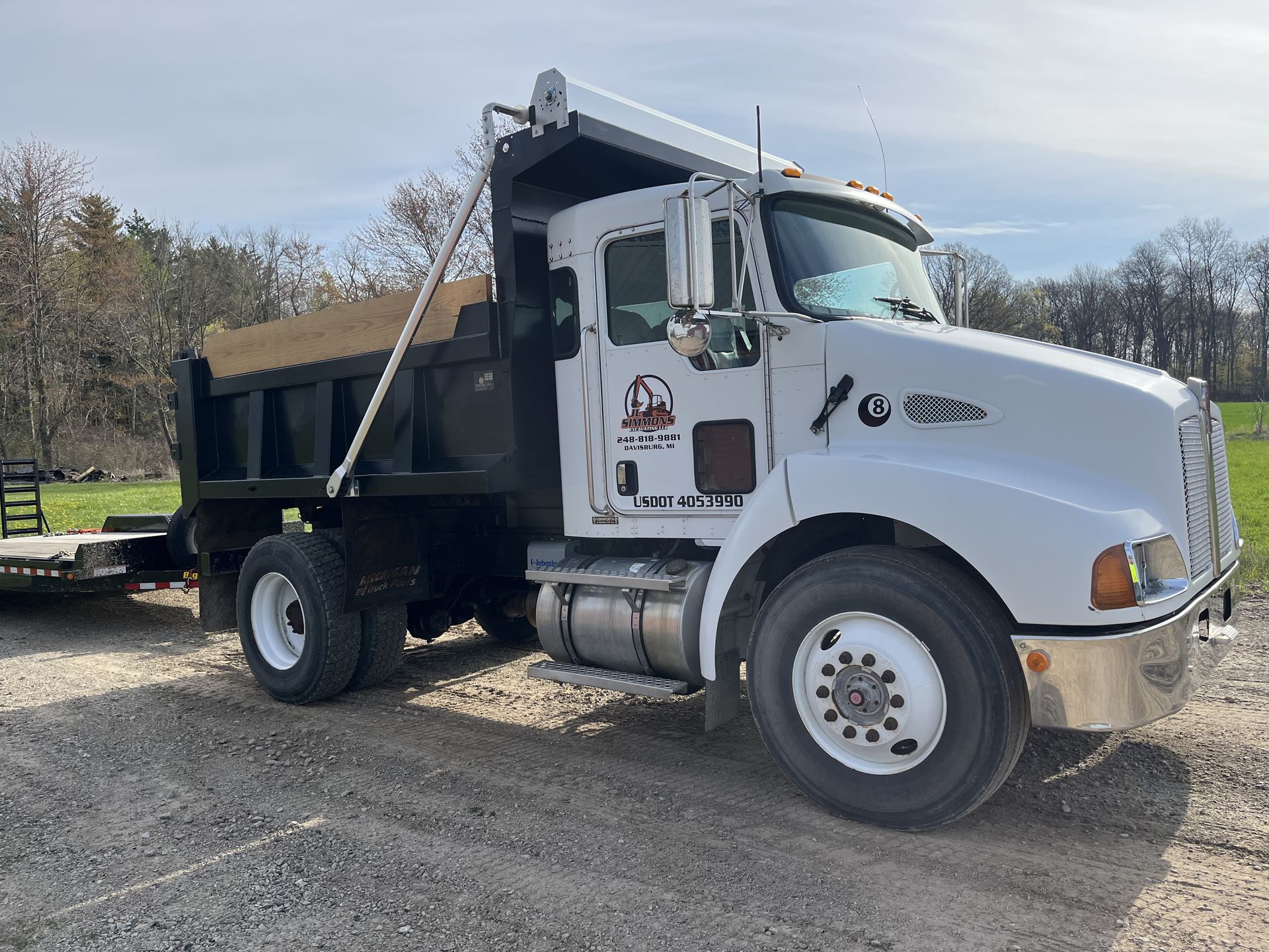 White dump truck parked on a gravel lot beside trees and a bench