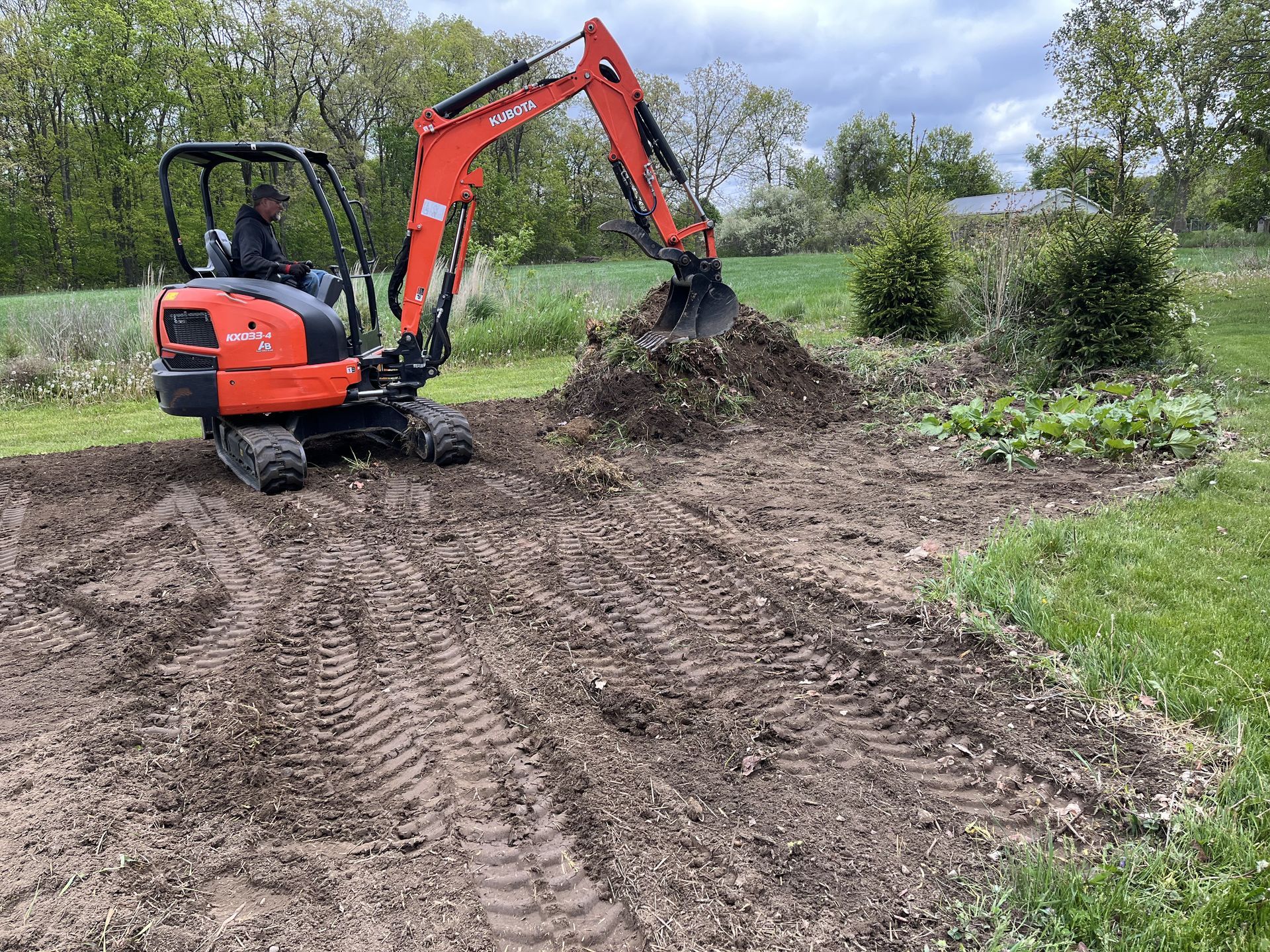 Orange excavator digging in a muddy field beside green vegetation