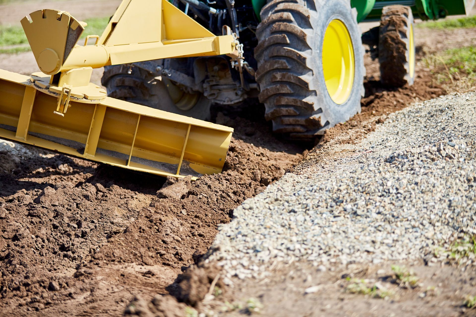 Yellow construction vehicle grading dirt beside a gravel path