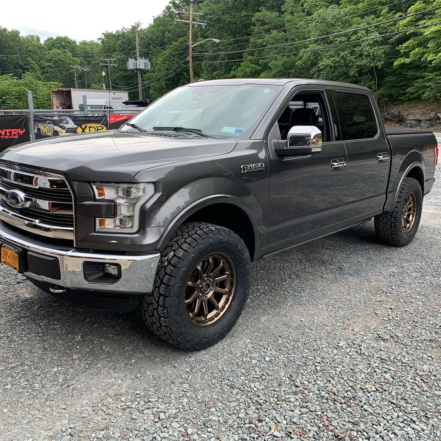 Gray Ford F-150 pickup truck with bronze wheels parked on gravel, in front of a building. Gray Ford F-150 pickup truck with bronze wheels parked on gravel, in front of a building.