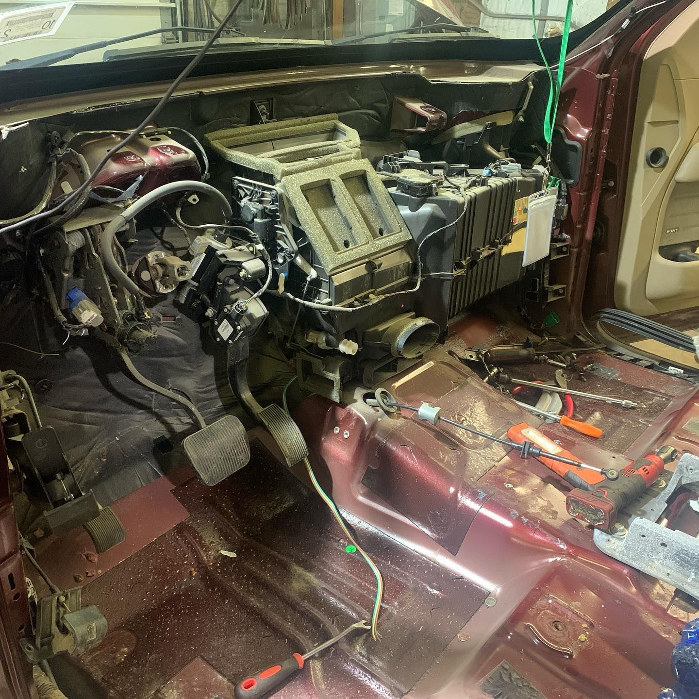 Interior of a car with dashboard components removed, revealing air conditioning system, wires, and tools on a maroon floor. Interior of a car with dashboard components removed, revealing air conditioning system, wires, and tools on a maroon floor.